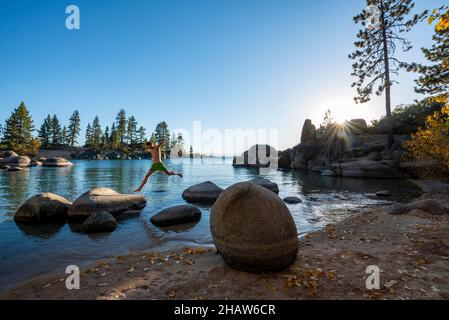 Un jeune homme dans des troncs de natation saute de pierre à pierre, des pierres rondes dans l'eau, la baie au lac Tahoe, plage de Sand Harbor, parc national de Sand Harbor Banque D'Images