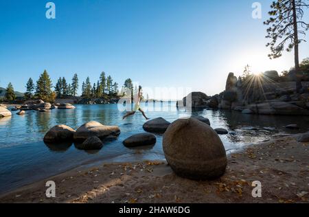 Un jeune homme dans des troncs de natation saute de pierre à pierre, des pierres rondes dans l'eau, la baie au lac Tahoe, plage de Sand Harbor, parc national de Sand Harbor Banque D'Images