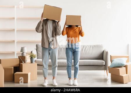 Un jeune couple stupide se baladant avec des boîtes en carton sur leur tête dans un nouvel appartement le jour de déplacement, l'espace de copie Banque D'Images