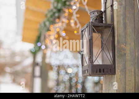 Lanterne en fer de rue antique suspendue sur le poteau en bois d'une maison décorée avec des guirlandes lumineuses à l'extérieur Banque D'Images