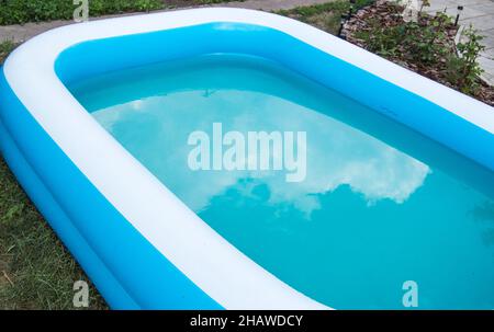 Gros plan d'une piscine gonflable debout sur l'herbe un jour ensoleillé d'été, le reflet des nuages à la surface de l'eau. Banque D'Images