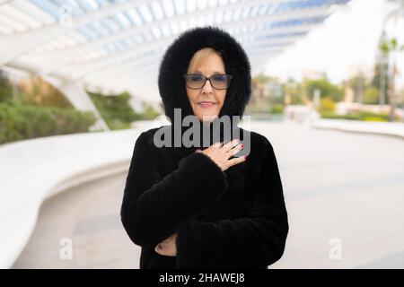 Femme élégante, souriante et sénior, en manteau noir élégant posé en ville.Concept d'hiver. Banque D'Images