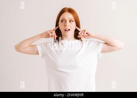 Portrait de la jeune femme mécontenté couvrant ses oreilles et gesticting dire pas de bla-bla-bla debout sur fond blanc isolé dans le studio. Banque D'Images