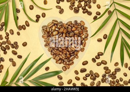 Composition écologique avec grains de café bio sur papier artisanal en forme de coeur avec feuilles de palmier sur fond artisanal.Concept de naturel Banque D'Images