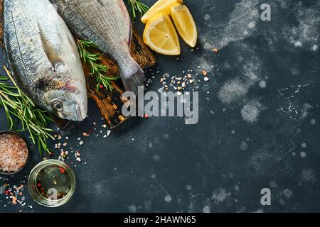 dorado cru poisson frais ou dorade de mer avec des ingrédients pour faire citron, thym, ail, tomate cerise et sel sur une ardoise noire, pierre ou fond de béton Banque D'Images