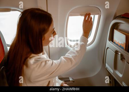 Jeune femme qui ferme la fenêtre pendant le vol à bord de l'avion Banque D'Images