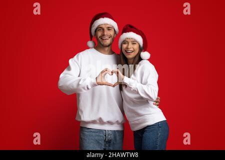 Couple Jeune romantique à Santa Hats faisant le symbole du coeur avec leurs mains Banque D'Images
