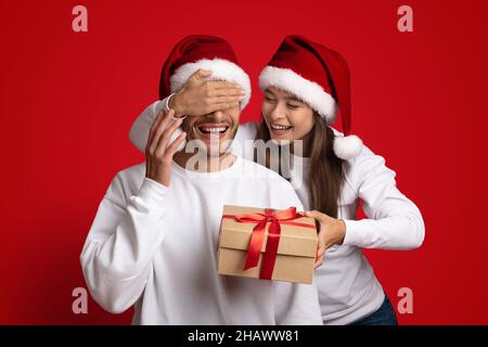 Cadeau pour vous.Une femme au chapeau de père Noël fait la surprise de Noël à Boyfriend Banque D'Images