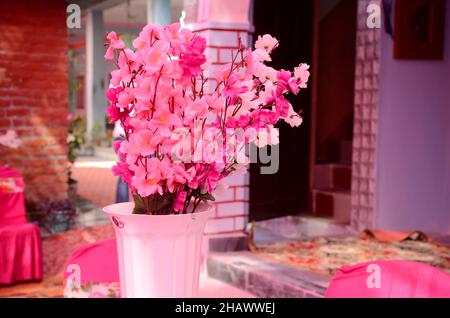 gros plan la fleur blanche rose artificielle dans le pot blanc sur un fond brun rose hors foyer. Banque D'Images