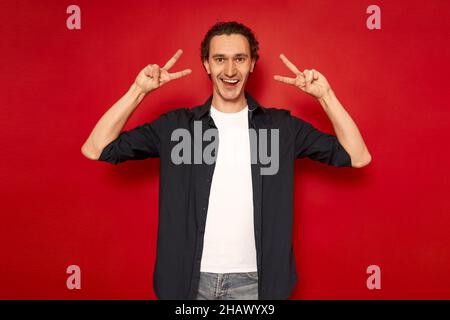 portrait beau sourire, jeune homme mûr habillé de chemise bleue avec des signes souriants en forme de v Banque D'Images