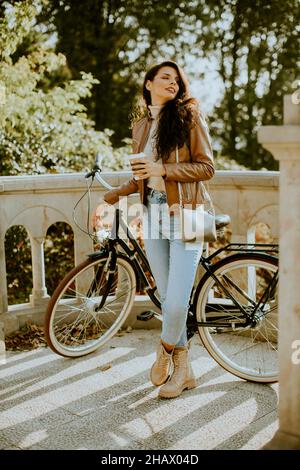 Jolie jeune femme tenant une tasse de café à emporter à vélo le jour de l'automne Banque D'Images