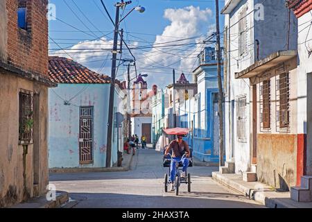 Bicitaxi / vélo taxi à travers la rue étroite avec des maisons colorées dans le centre de la vieille ville de Camagüey sur l'île de Cuba, les Caraïbes Banque D'Images