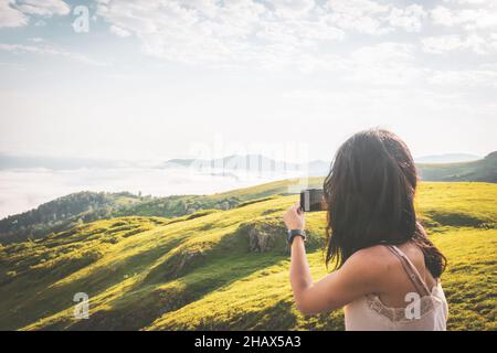 Vue rapprochée de l'arrière de la femme brunette prenant la photo de smartphone des vues pittoresques de prairie de rêve Banque D'Images