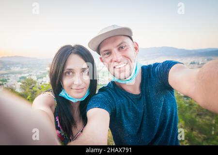 gros plan sur des visages masculins et féminins avec des masques en retrait tout en prenant un selfie portable avec vue panoramique sur la ville en arrière-plan.Nouvelle normale Banque D'Images