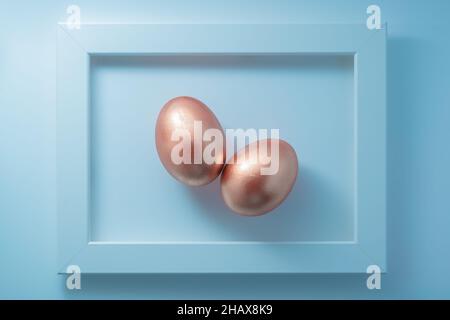 Paire d'œufs dorés encadrés sur fond bleu pastel.Œuvres d'art contemporain composition de pâques.Flat lay, vue de dessus, espace de copie. Banque D'Images