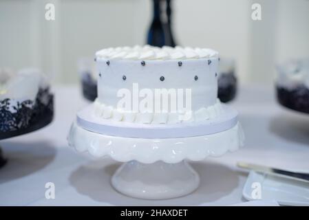 Un gâteau de mariage blanc plus tard avec de la dentelle comestible et des arrosettes argentées sur un moule à gâteau blanc en céramique Banque D'Images