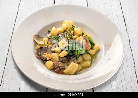 Boulettes de pommes de terre gnocchi avec palourdes et navets verts en plaque blanche sur table blanche en bois Banque D'Images