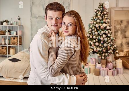 Date romantique le réveillon de Noël, un jeune couple amoureux s'embrasse près de l'arbre de Noël. Banque D'Images