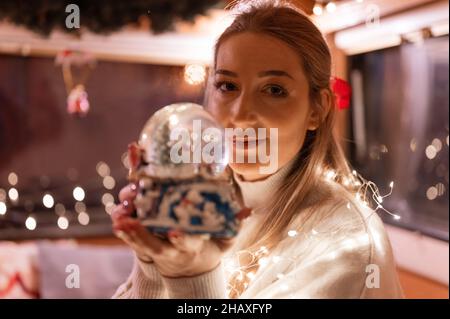 belle jeune femme en forme de chand tenant les mains près du visage et admirez le globe de neige ou le dôme en verre et profitez d'une ambiance relaxante et inspirante à la maison Banque D'Images