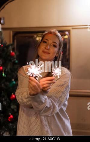 femme floue en laine tricotée blanc confortable sweat-shirt mains tenant des sparklers bengale bâton de feu sur le fond d'un camping remorque maison en extérieur sur neuf Banque D'Images