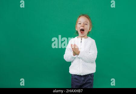 une petite fille hurle fort avec sa bouche large ouverte sur un fond vert isolé Banque D'Images