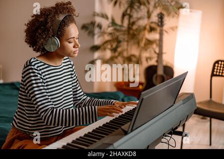 Jeune femme dans un casque jouant au synthétiseur à la maison Banque D'Images