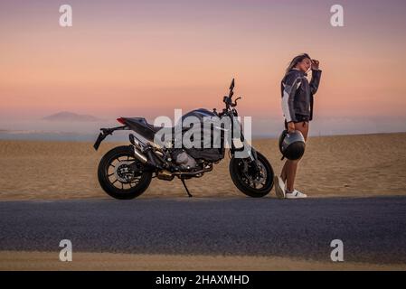 Motard femelle debout sur le côté de la route à côté de sa moto, Tarifa, Cadix, Andalousie, Espagne Banque D'Images