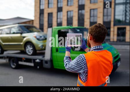 Un assistant de dépanneuse pour photographier une voiture chargée Banque D'Images