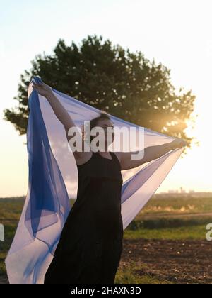 Femme debout dans un champ tenant un morceau de tissu au-dessus de sa tête, France Banque D'Images