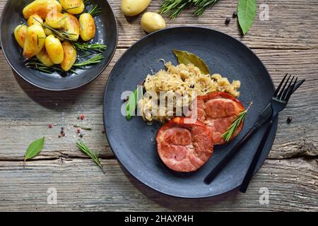 La cuisine allemande est un goulot de porc fumé avec de la choucroute et des pommes de terre frites servies sur une plaque en céramique sur une ancienne table en bois Banque D'Images