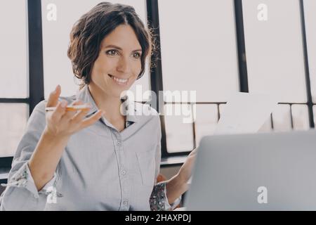 Gaie femme espagnole tuteur regarde l'écran d'ordinateur portable avec le sourire confiant tout en expliquant le nouveau sujet Banque D'Images