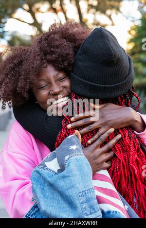 Jeunes amies afro-américaines joyeuses qui s'embrassent les unes les autres pendant qu'elles se trouvent dans le parc Banque D'Images