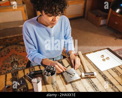 Angle élevé de l'artisan ethnique féminin assis à la table et préparant des instruments pour le travail d'orfèvre Banque D'Images