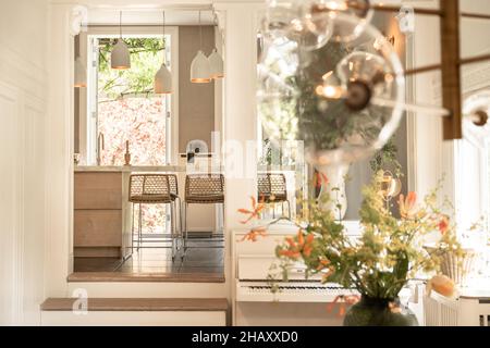 Intérieur de la salle de séjour classique avec bouquet de piano blanc de fleurs de champ dans vase en céramique et vue perspective à la cuisine avec comptoir avec évier et Banque D'Images