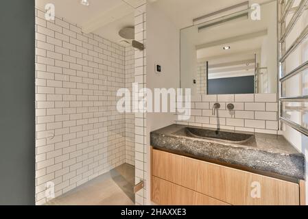 Salle de bains contemporaine dans la chambre avec lavabo et robinet avec armoire porte-serviettes chauffant miroir et cabine de douche avec mur en brique Banque D'Images