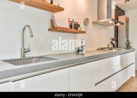 Intérieur de la grande salle de cuisine claire et étroite meublée avec des armoires en bois blanc avec cuisinière à gaz et ustensiles à la lumière du jour Banque D'Images