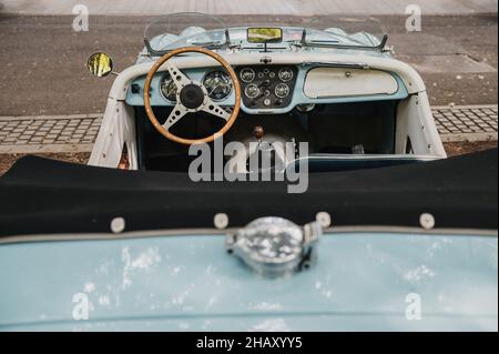 Vieille voiture décapotable avec miroirs et tableau de bord de style rétro garée sur une rue pavée près de la route asphaltée de la ville Banque D'Images