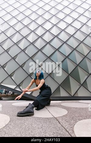 Jeune femme aux cheveux bleus dans une tenue noire, dansant contemporaine près d'un bâtiment moderne sur la rue de la ville Banque D'Images