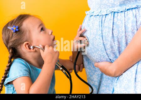 Maternité, chaud été - portrait tordu mère enceinte femme méconnaissable robe bleue petite fille fille frère traiter maman jeu de rôle Banque D'Images