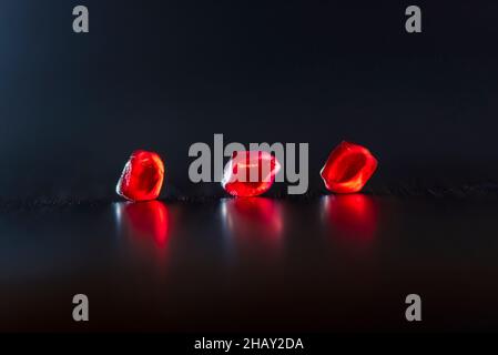 Gros plan de fruits de grenade mûrs juteux rouge vif et brillant placés sur fond sombre Banque D'Images