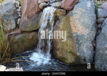 Une petite chute d'eau qui se déforme au-dessus de rochers et de petits rochers et qui atterrit dans un petit bassin d'eau aux jardins de Sinnississspi à Rockford, Illinois Banque D'Images