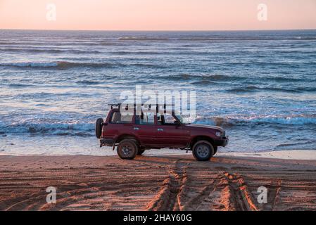 Voiture offroad rouge garée sur le rivage sur le sable à la plage en soirée Banque D'Images