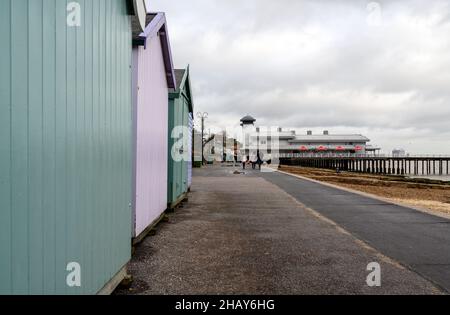 Felixstowe, Suffolk, Royaume-Uni: Les gens marchent le long de la promenade Felixstowe pendant une journée froide et terne d'hiver, après une ligne de cabanes de plage et de la jetée. Banque D'Images