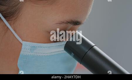 Biologiste avec masque facial utilisant une lentille microscopique sur un outil de chimie en laboratoire.Ingénieur scientifique utilisant un microscope avec loupe et une focalisation sélective pour travailler sur des expériences de laboratoire. Banque D'Images