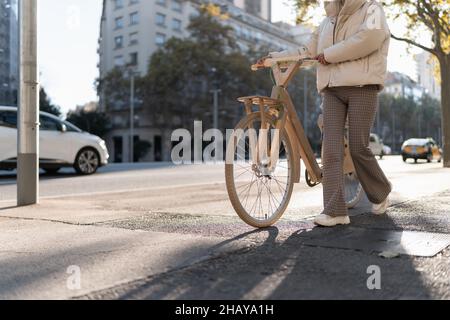 Petite femme élégante avec vélo en bois marchant sur le chemin de l'asphalte près de la route le jour ensoleillé en ville. Banque D'Images