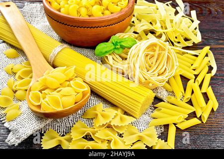 Pâtes de coquillages dans une cuillère, tuyau de rigate dans un bol, spaghetti, tagliatelle, penne, farfalle,trancheuse sur toile de fond en bois Banque D'Images