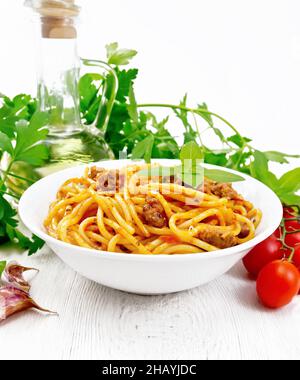 Pâtes spaghetti à la sauce Bolognese de viande hachée, jus de tomate, ail, vin et basilic dans une assiette, huile végétale, herbe épicée sur un sanglier blanc en bois Banque D'Images