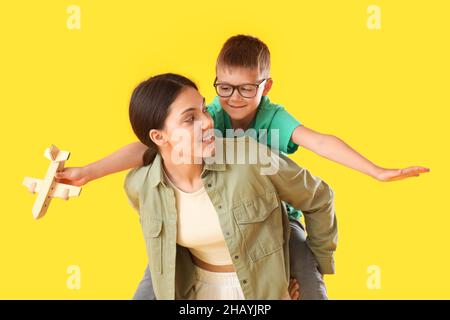 Adolescente transportant un pickaback son petit frère avec un avion en bois sur fond jaune Banque D'Images