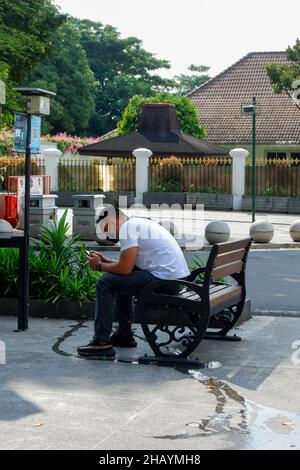 yogyakarta, Indonésie - novembre 20 2021 : des hommes sont assis sur les sièges fournis dans le centre-ville tout en jouant au téléphone portable pendant la journée Banque D'Images