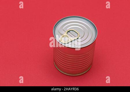 Boîte en étain non ouverte avec bord vierge sur fond rouge.Aliments en conserve.Boîte en aluminium pour un stockage sûr et à long terme des aliments.Conteneur d'entreposage des aliments scellé en acier Banque D'Images